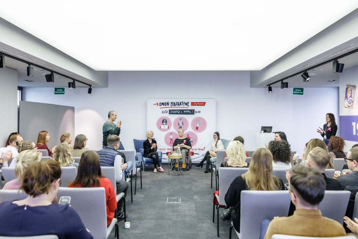 Uczestnicy wydarzenia edukacyjnego „Zmień perspektywę” siedzą w sali konferencyjnej i słuchają panelu prowadzonego przez zespół Fundacji TAKpełnosprawni. Spotkanie dotyczy doświadczenia niepełnosprawności i dostępności w miejscu pracy.