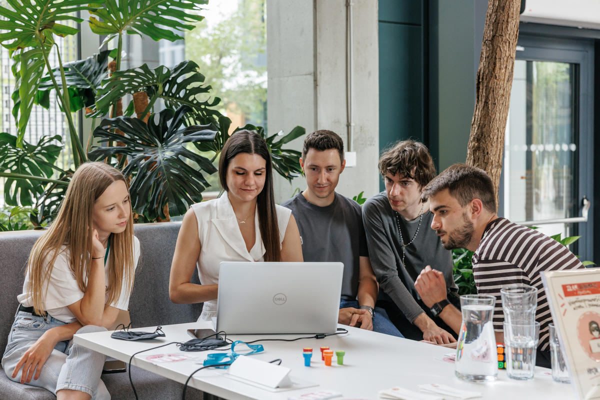 Five people are sitting at a table with a laptop, analyzing material together. On the table are accessibility training accessories.