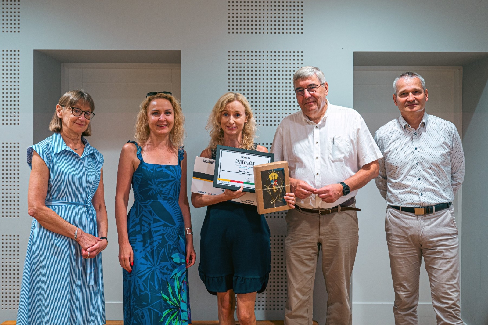 A group of five posing with the “Initiator of the Year 2023” award. In the center, Agata Robińska holds certificates and a gift.